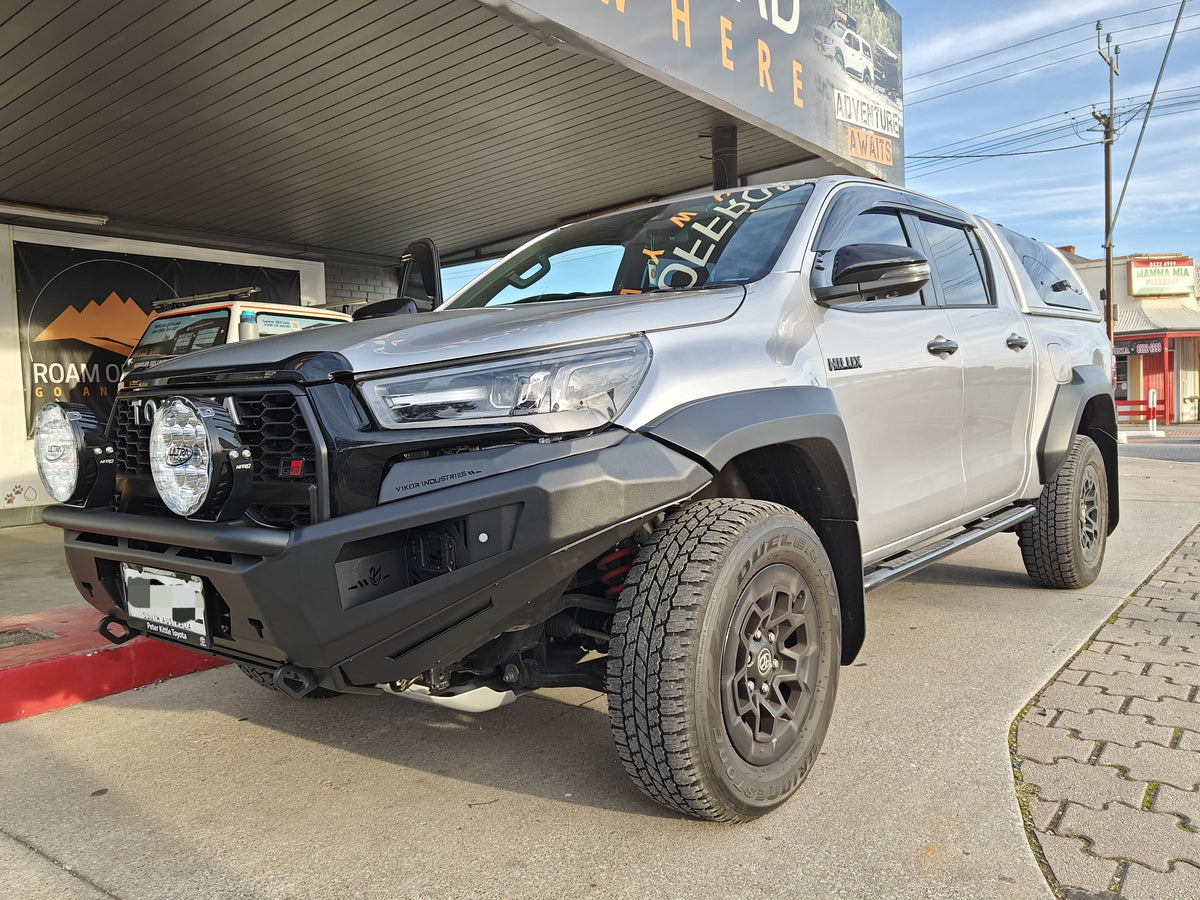 Silver Toyota Hilux with a black bull bar, round driving lights and red recovery points