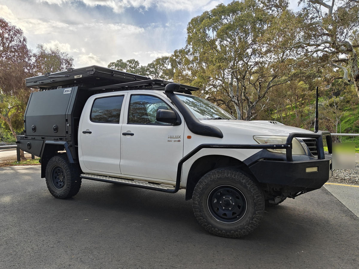 White Toyota Hilux with a black canopy, rooftop tent, snorkel and bull bar