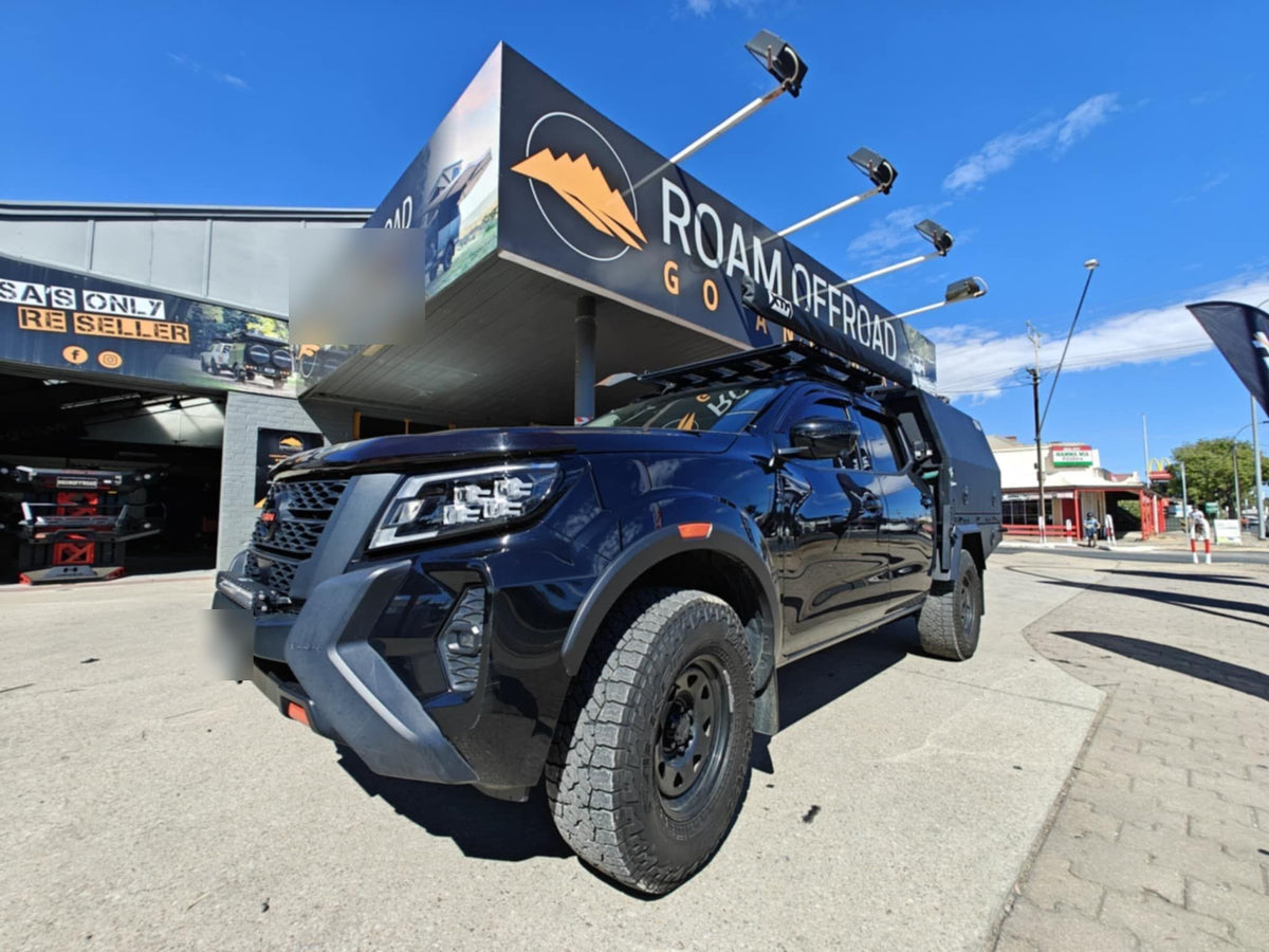 Black Nissan Navara with a bull bar and driving lights under the Roam Offroad sign